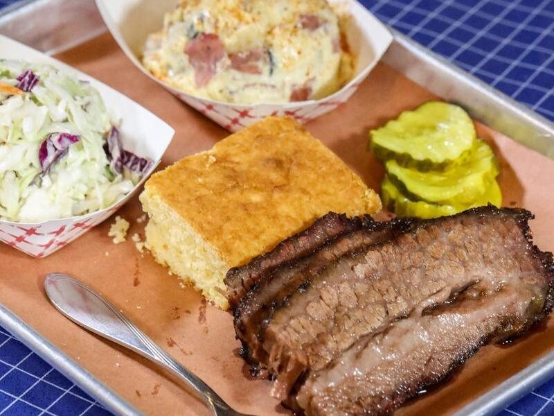 Sliced smoked beef brisket with cornbread, pickles, coleslaw and potato salad