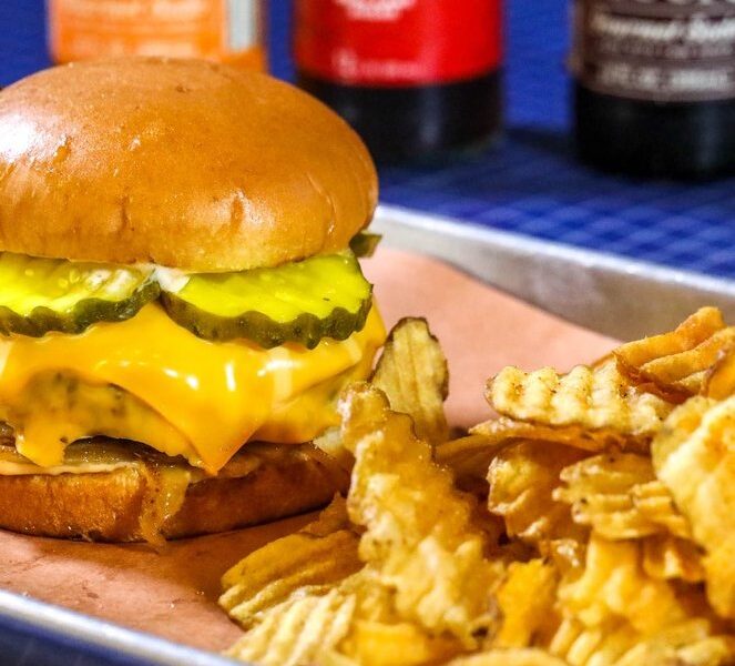 The CK Smoke House Burger with melted cheese and pickles next to house-fried chips